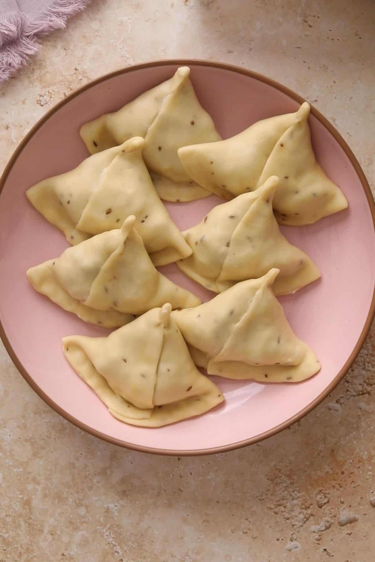 Samosa are shaped and placed on a shallow pink bowl.