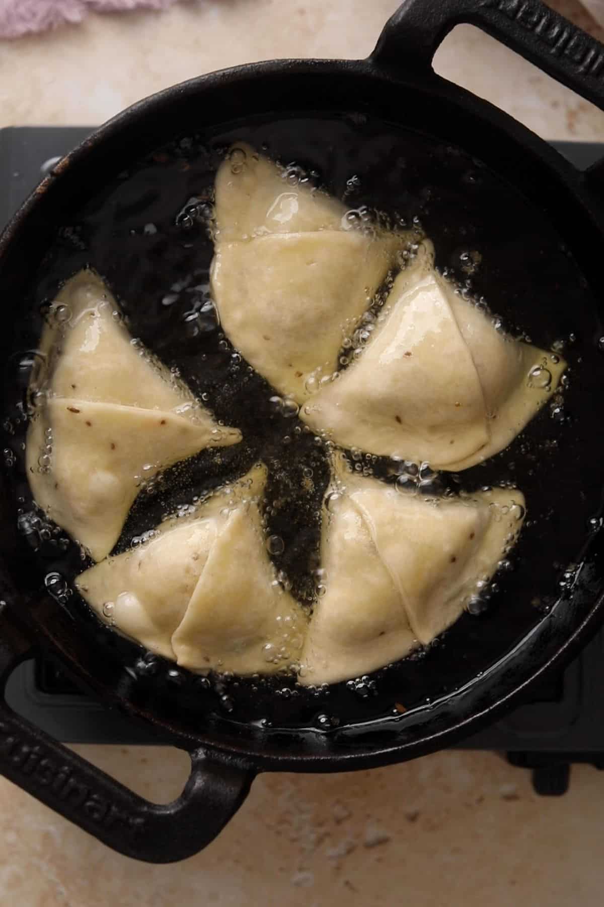 Samosas are frying in hot oil in a cast iron kadai.