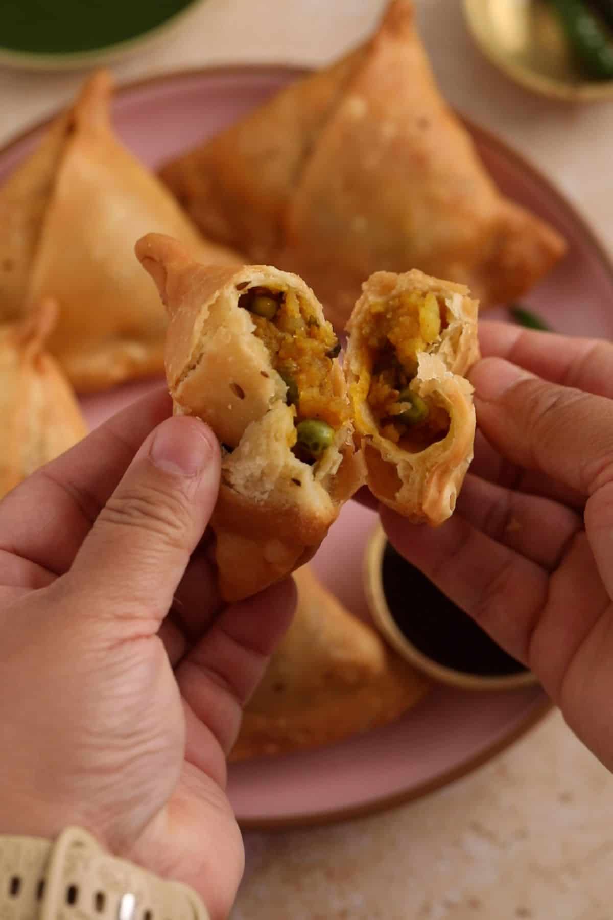 A samosa is break open to show the flaky crust and the potato pea filling.