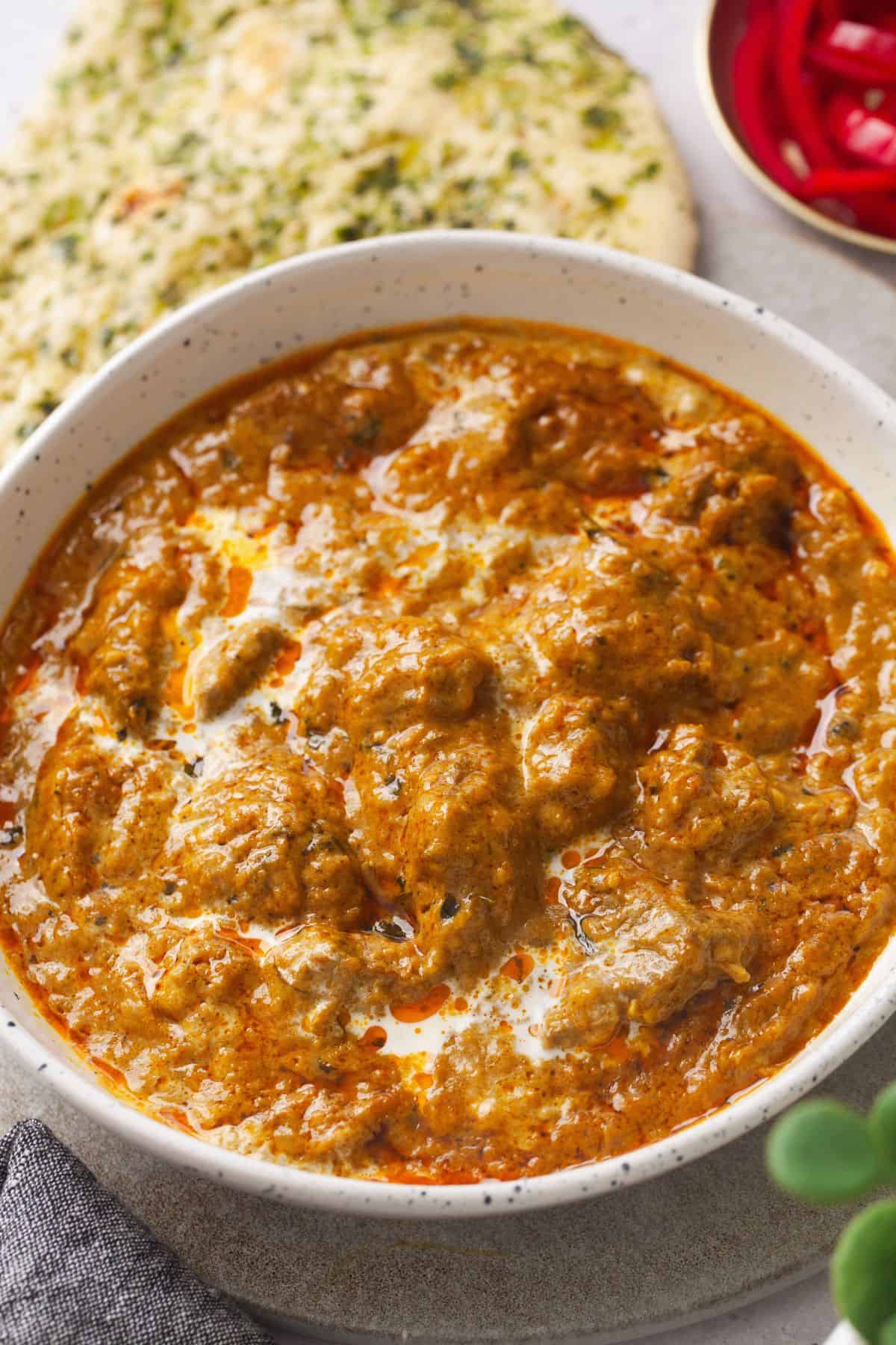 An angled view of lamb kprma curry with naan in background.