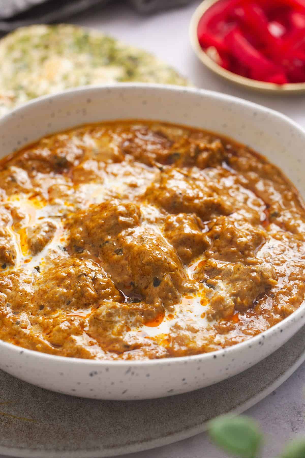 Side view of lamb korma in a specled white dish.