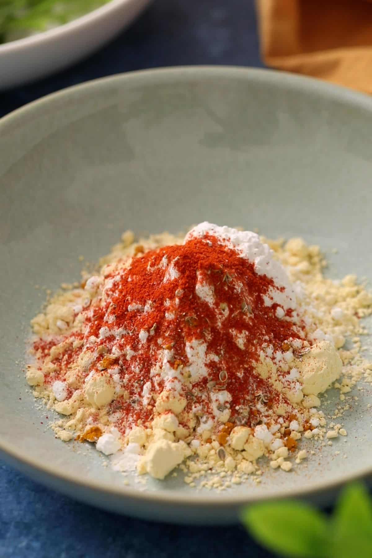 Gram flour, rice flour and spices in a shallow sea green bowl.