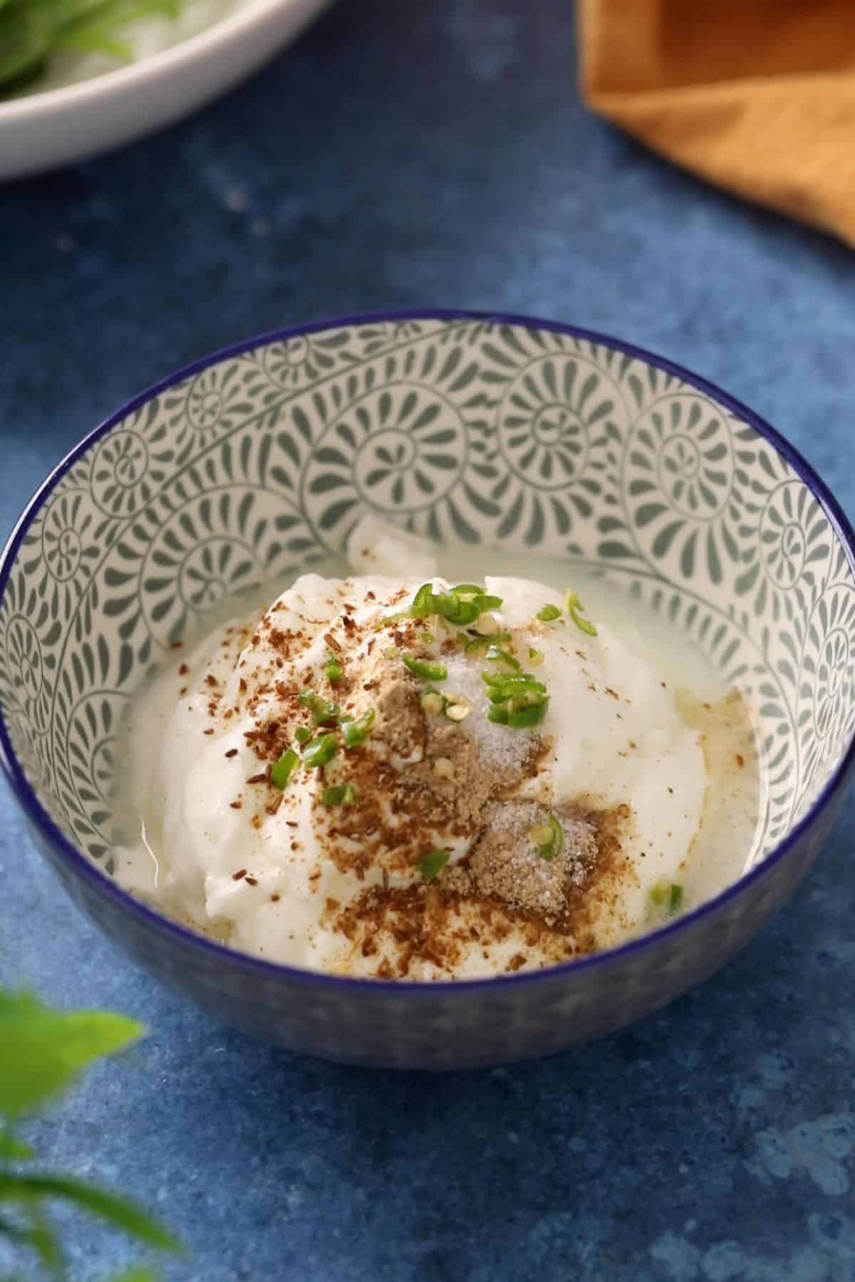 A blue bowl with yogurt, spices and green chillies.
