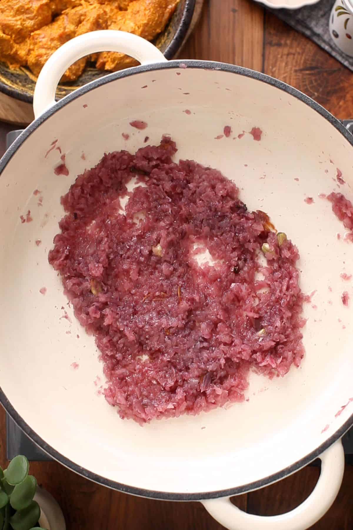 A white pot with sautéed finely chopped red onions, turning soft and translucent and light brown.