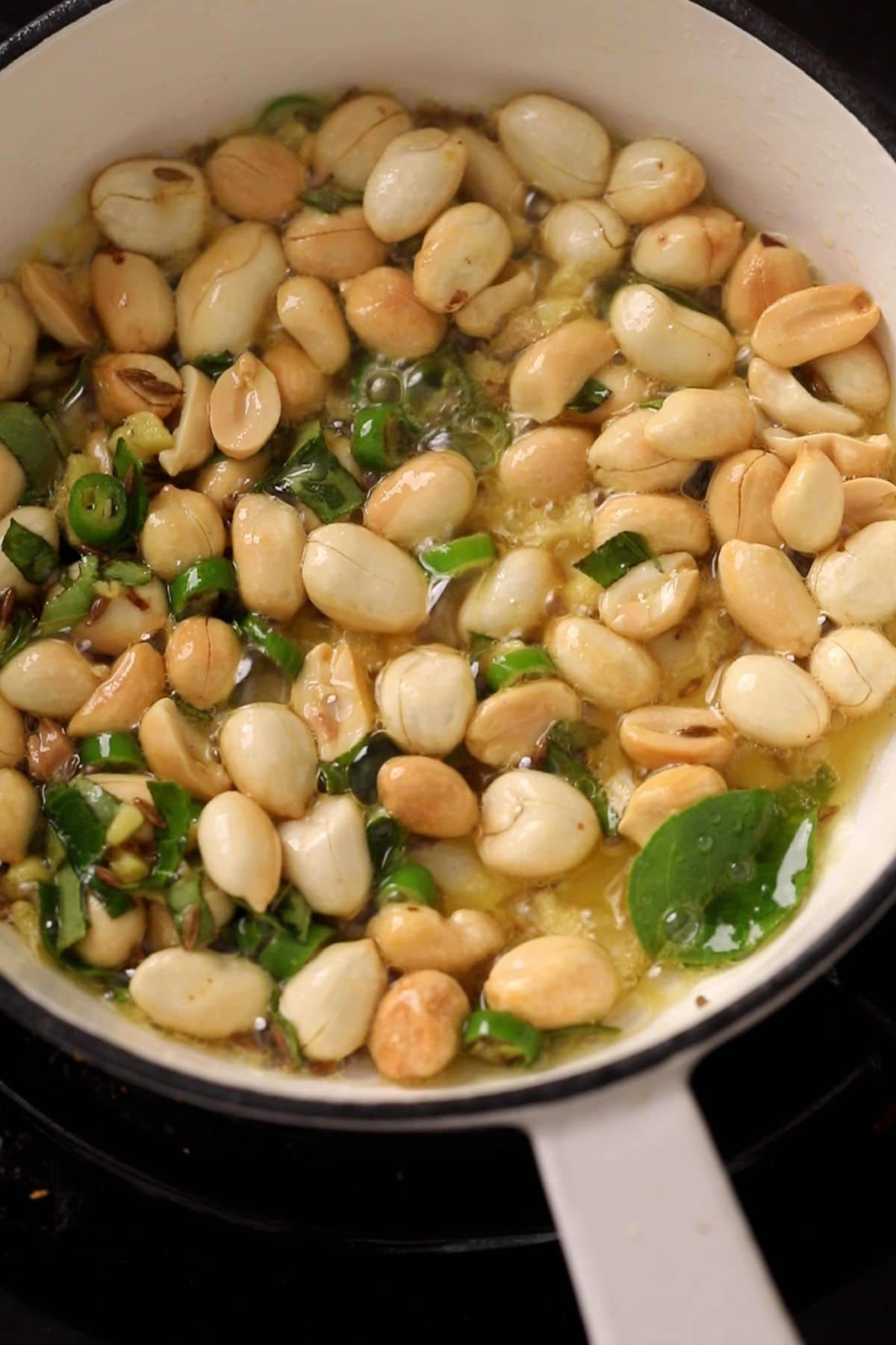 A small white pan with tempering made of peanuts, cumin and green chilies. 