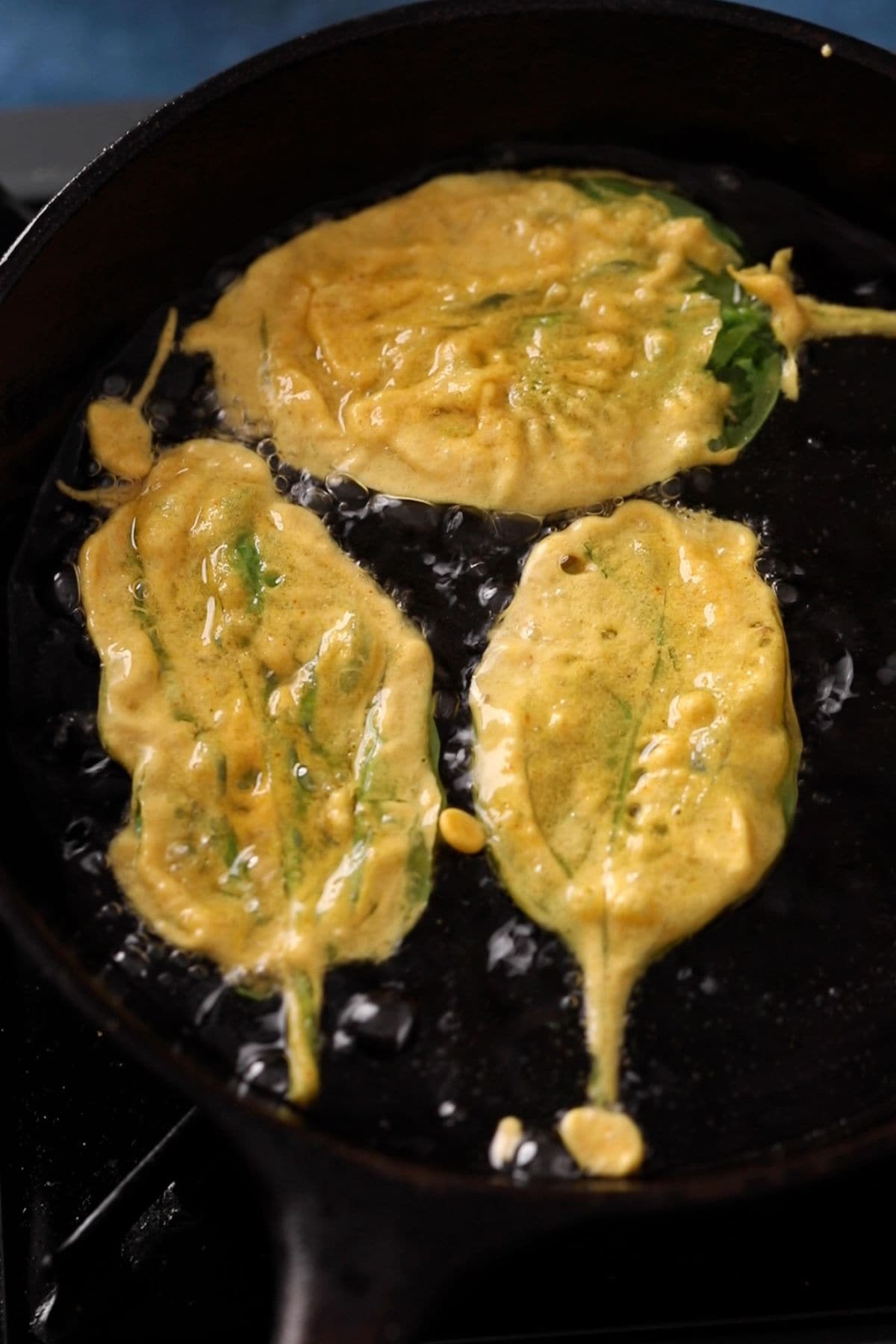 Battered spinach leaves are placed in hot oil.