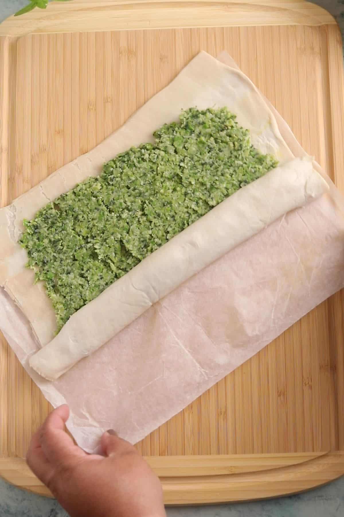 Puff pastry sheet is being rolled on a bamboo board.