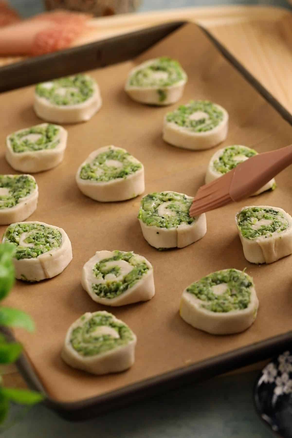 Pinwheels are arraged on a sheet, brished with butter and ready for baking.