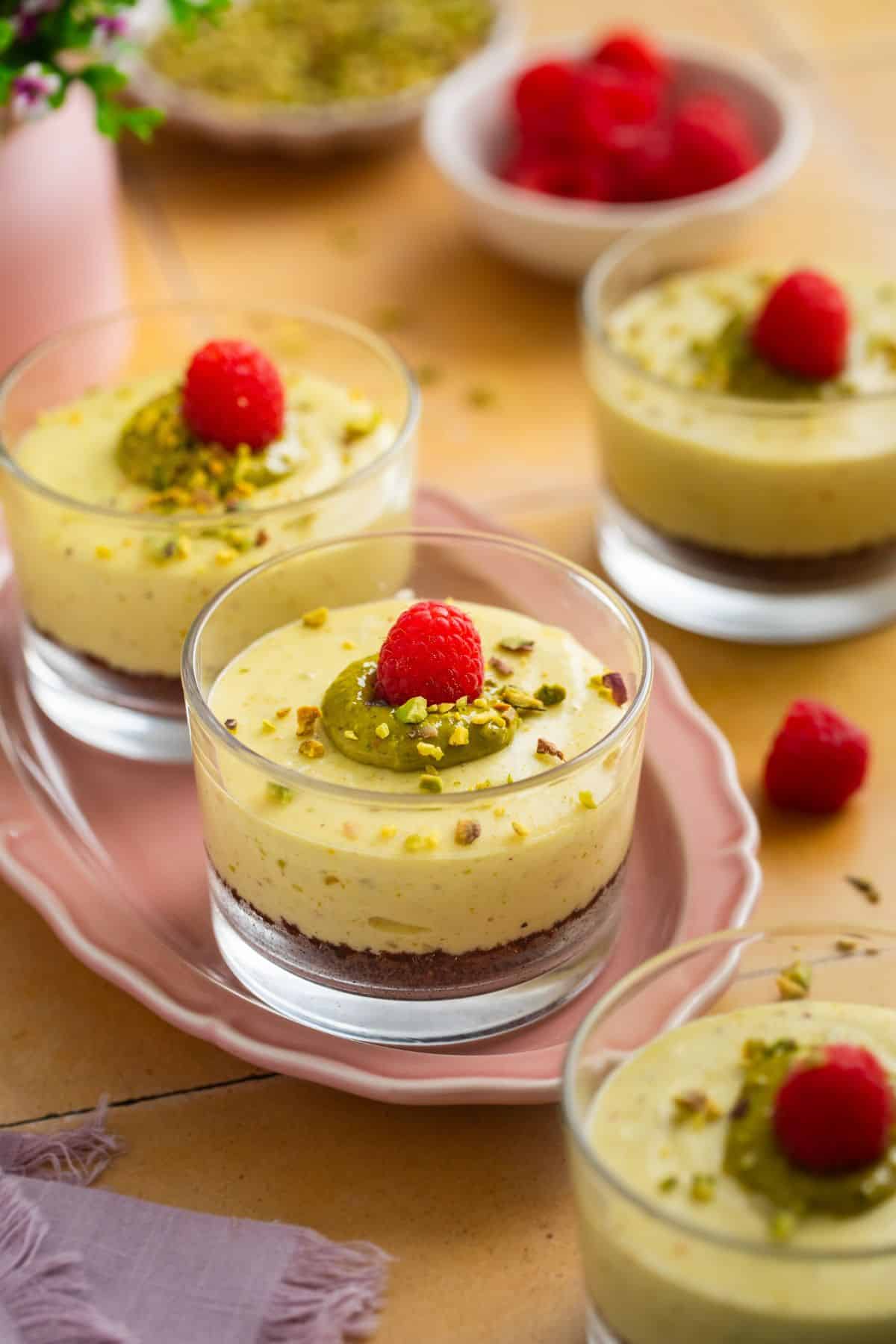 Pistachio Cheesecake cups placed on a pink tray wuth chpped pistachios in background.