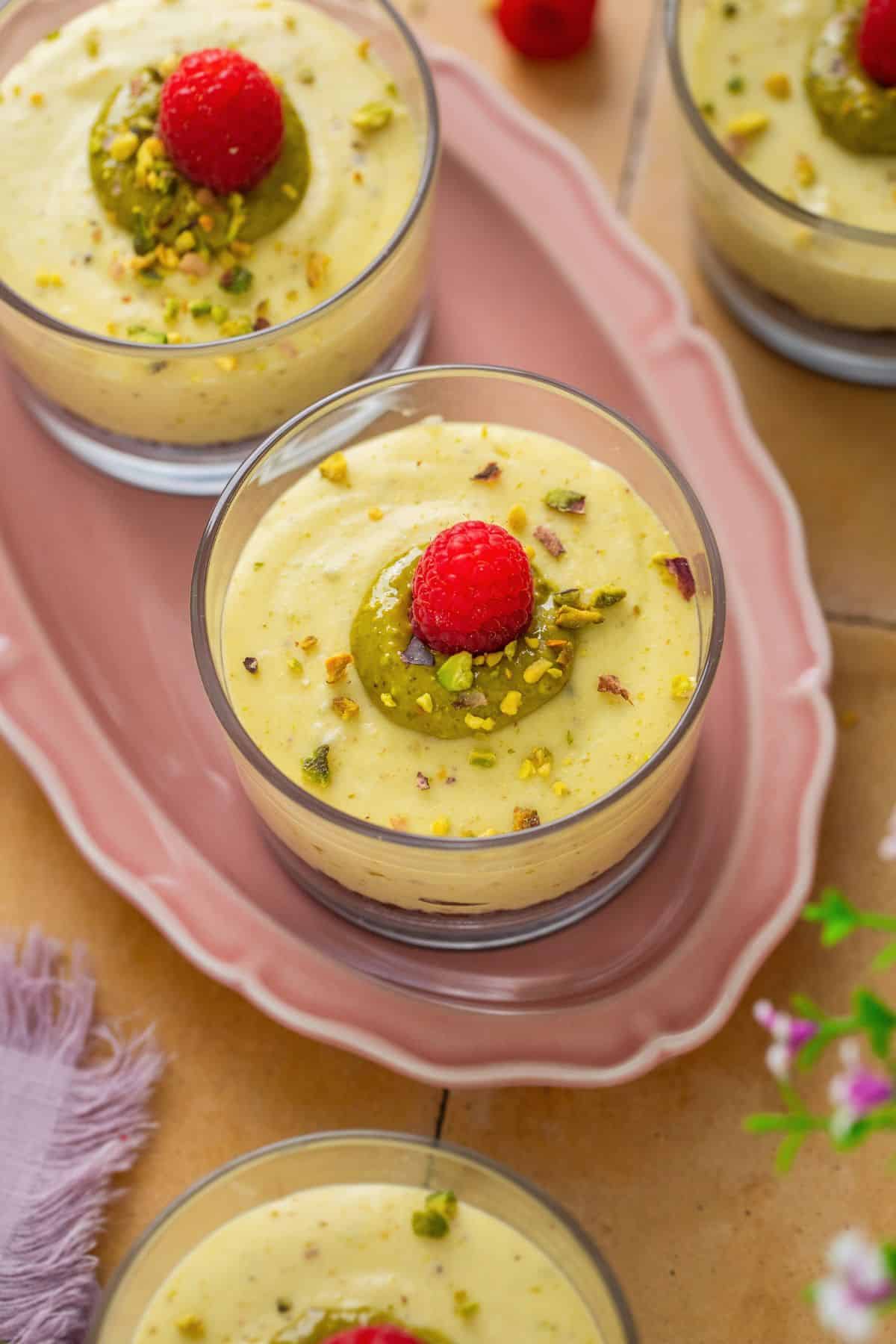 Pistachio cheesecake cups decorated with pistachio ceam and raspberries. 