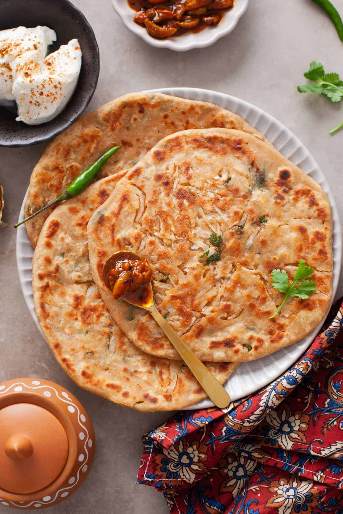 Mooli paratha served on a white plate with garlic pickle and yogurt on side. 