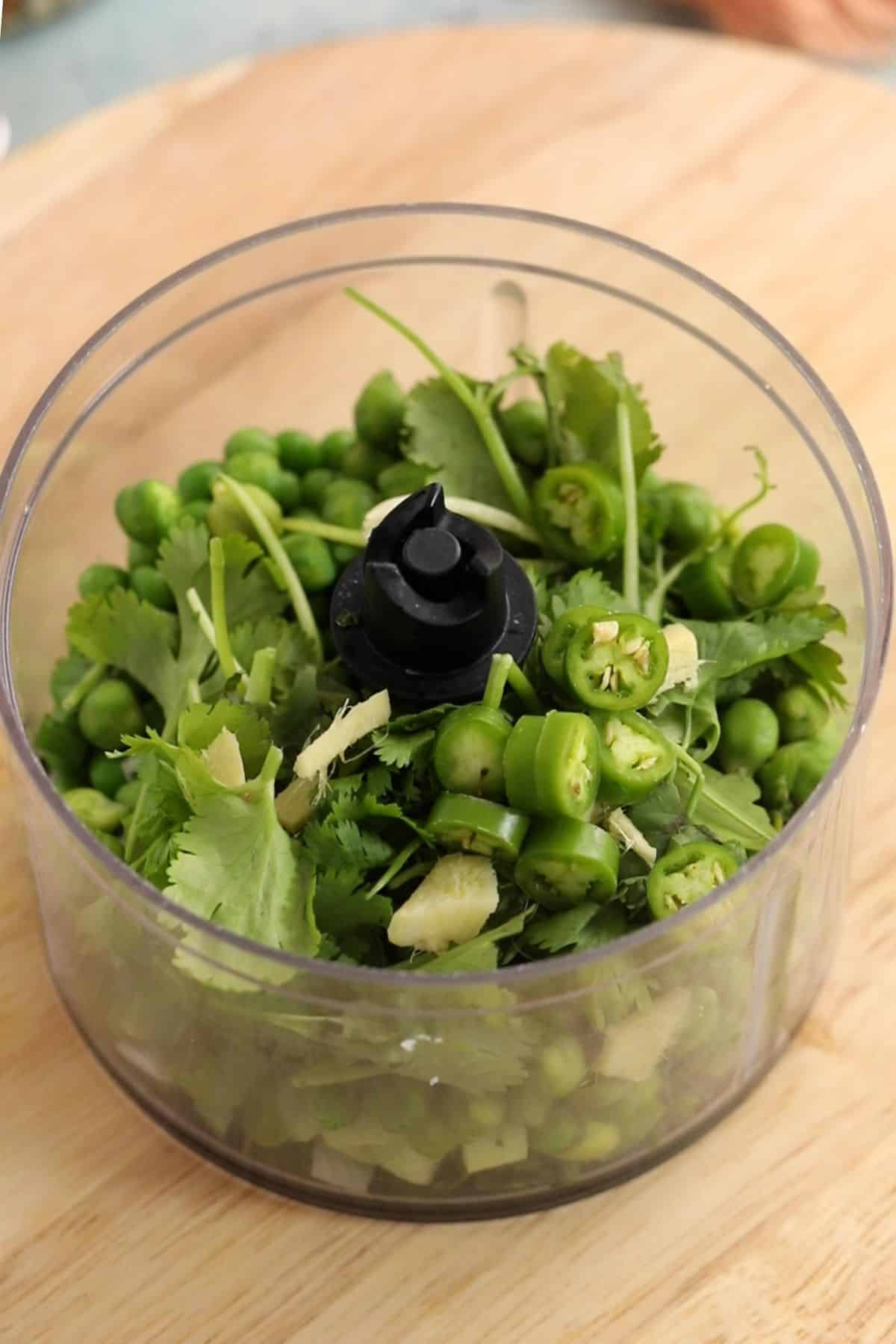 Green vegetables and aromatics in a small processor jar.