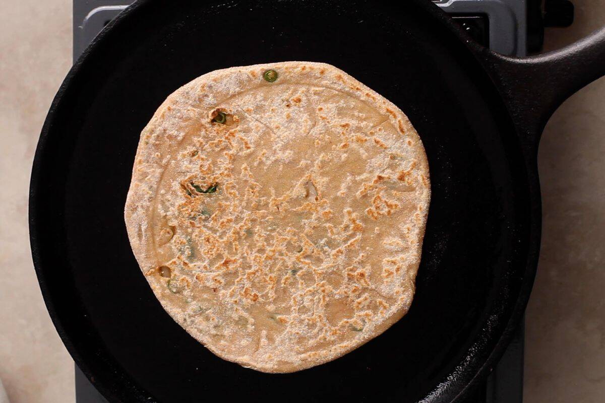 Paratha is cooked on a cast iron griddle. 