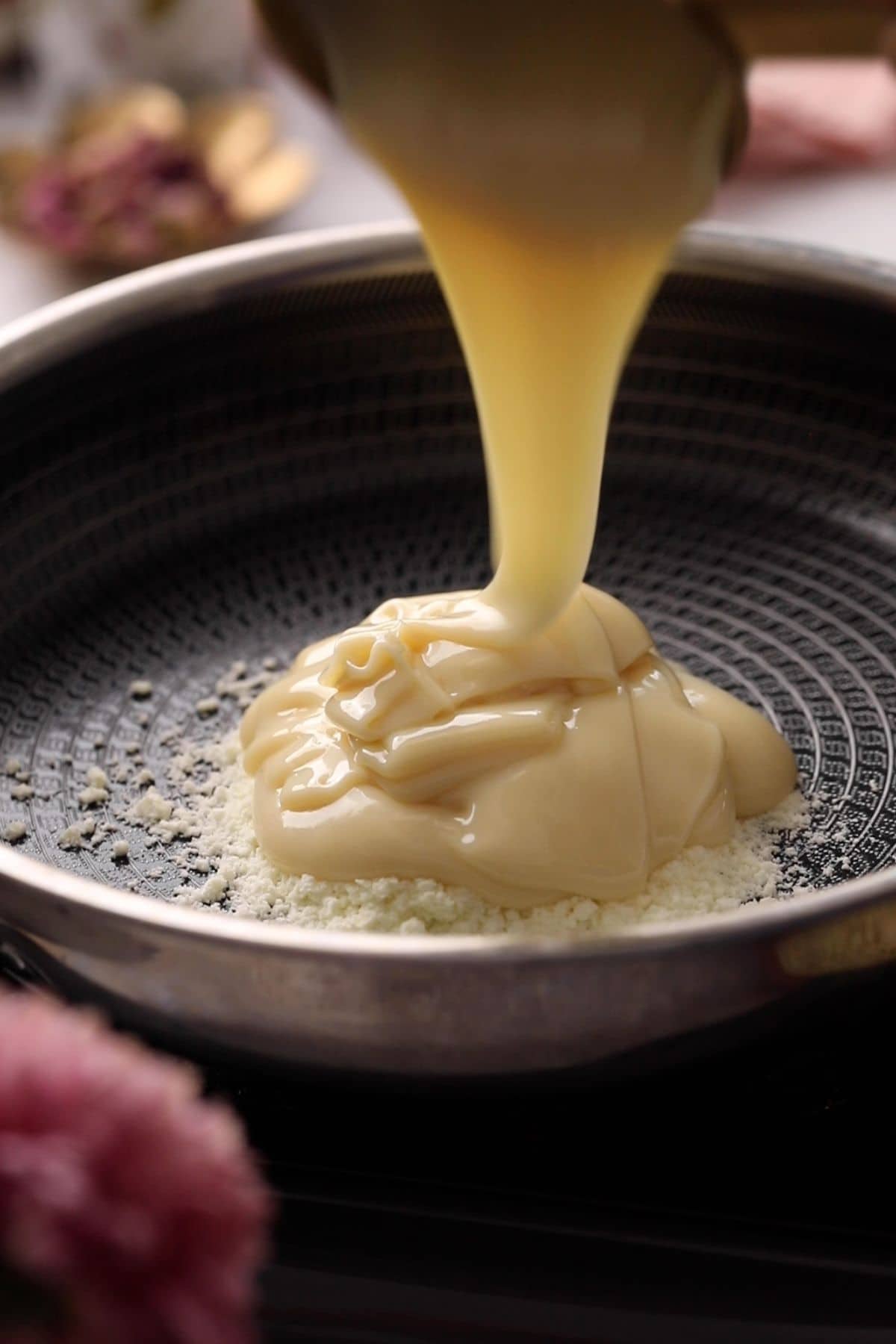Condensed milk is added to milk powder in a black pan.