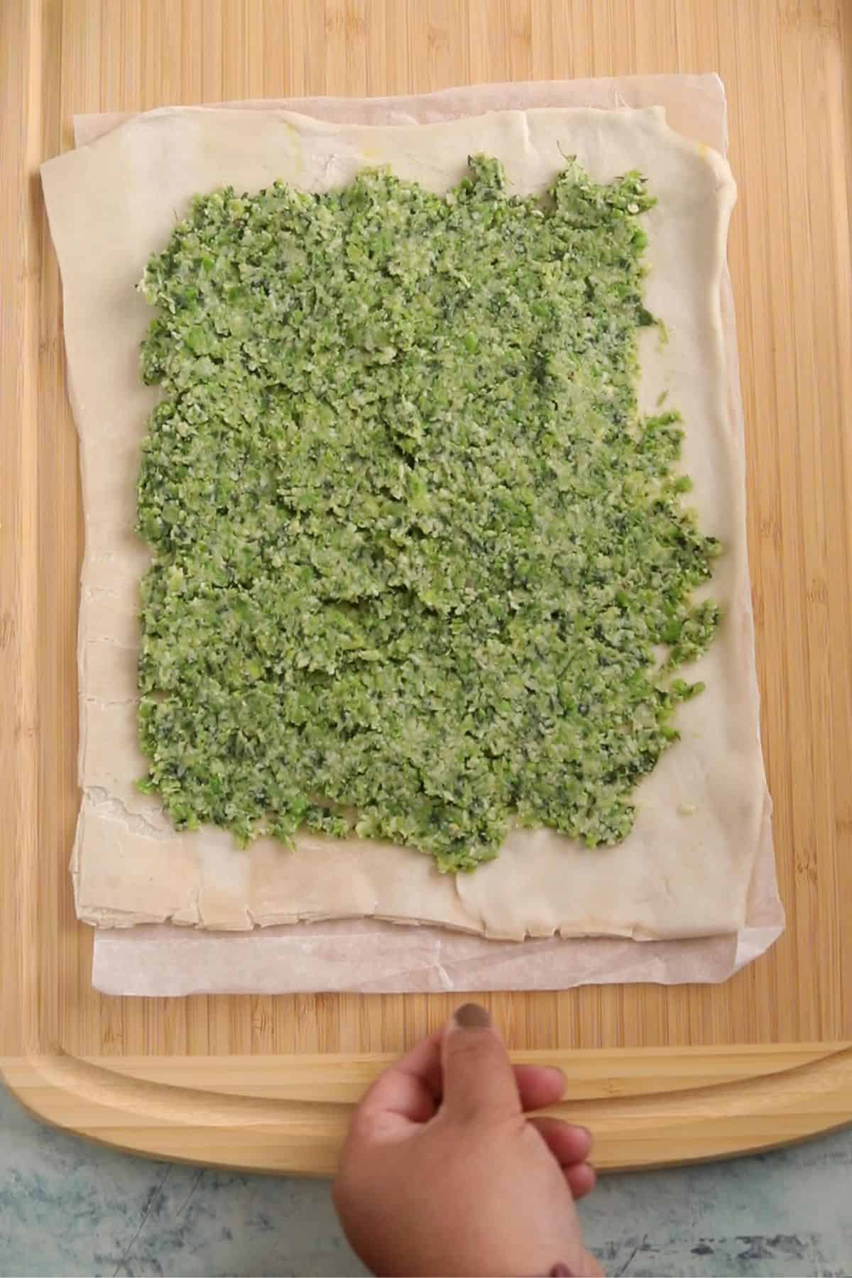 Hara bhara paste is spread on a puff pastry sheet placed on a bamboo board.