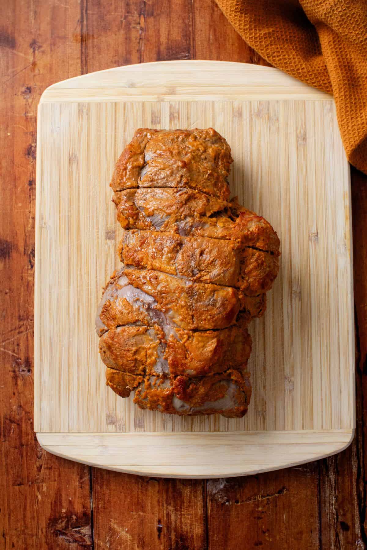 Boneless lamb leg roast rests on a bamboo board on a wooden background.