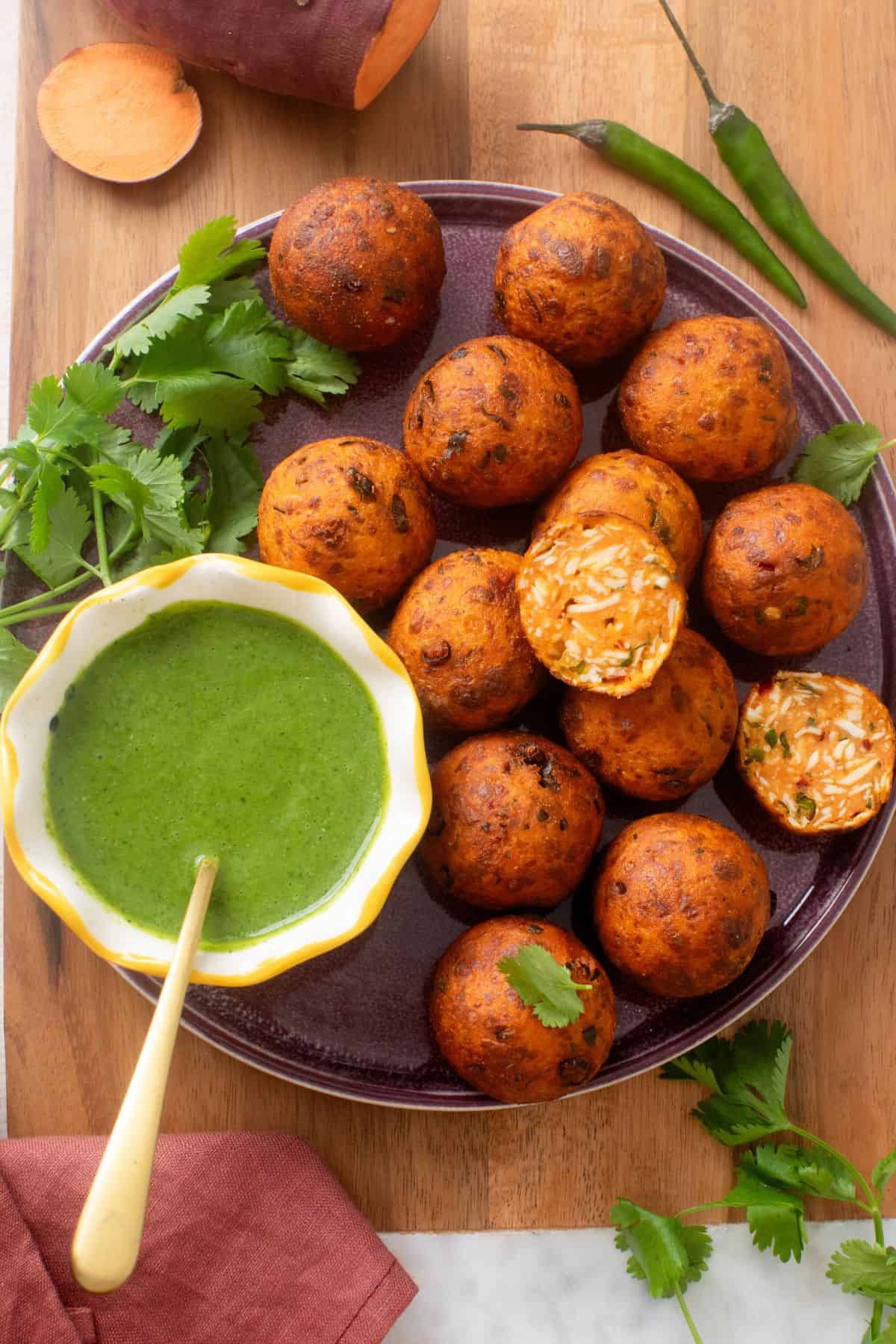 Overhead image of sweet potato kofta balls sweved in a purple plate with fresh cilantro, green chutney and green chilles. 