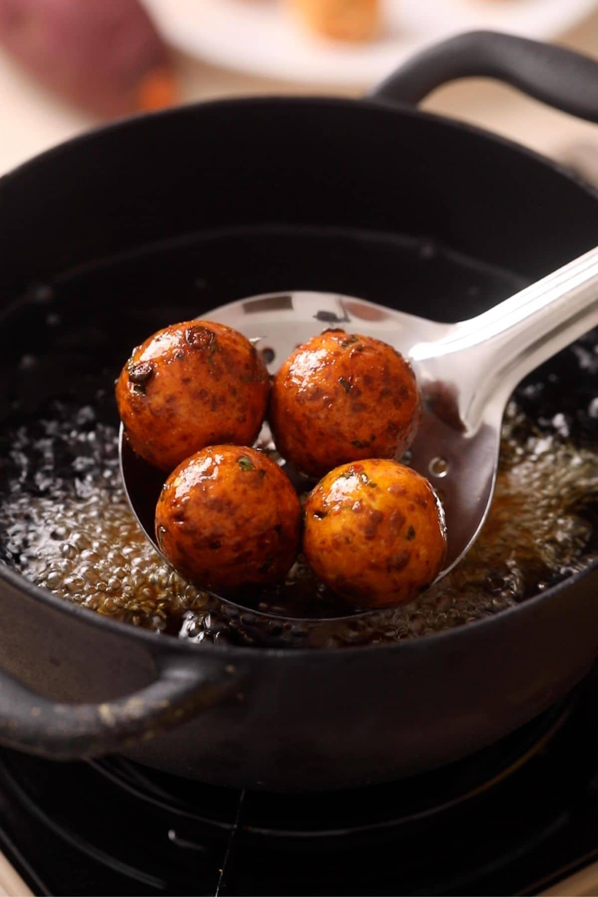Deep fried sweet potato kofta balls are in a stainer over a hot pot of oil. 